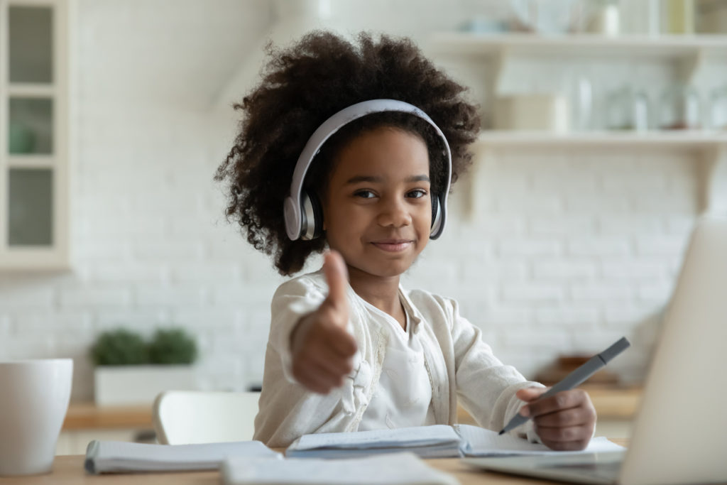 African-girl-in- headphones-enjoy-e-learn-sit-at-table- showing-thumbs-up- recommend-virtual-school