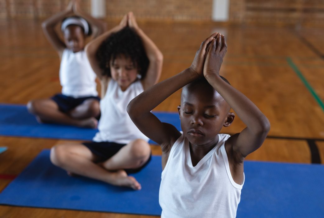 Schoolkids doing yoga and meditating on a yoga mat in school