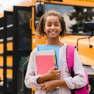 Smiling african-american schoolgirl going back to school with books and copybooks